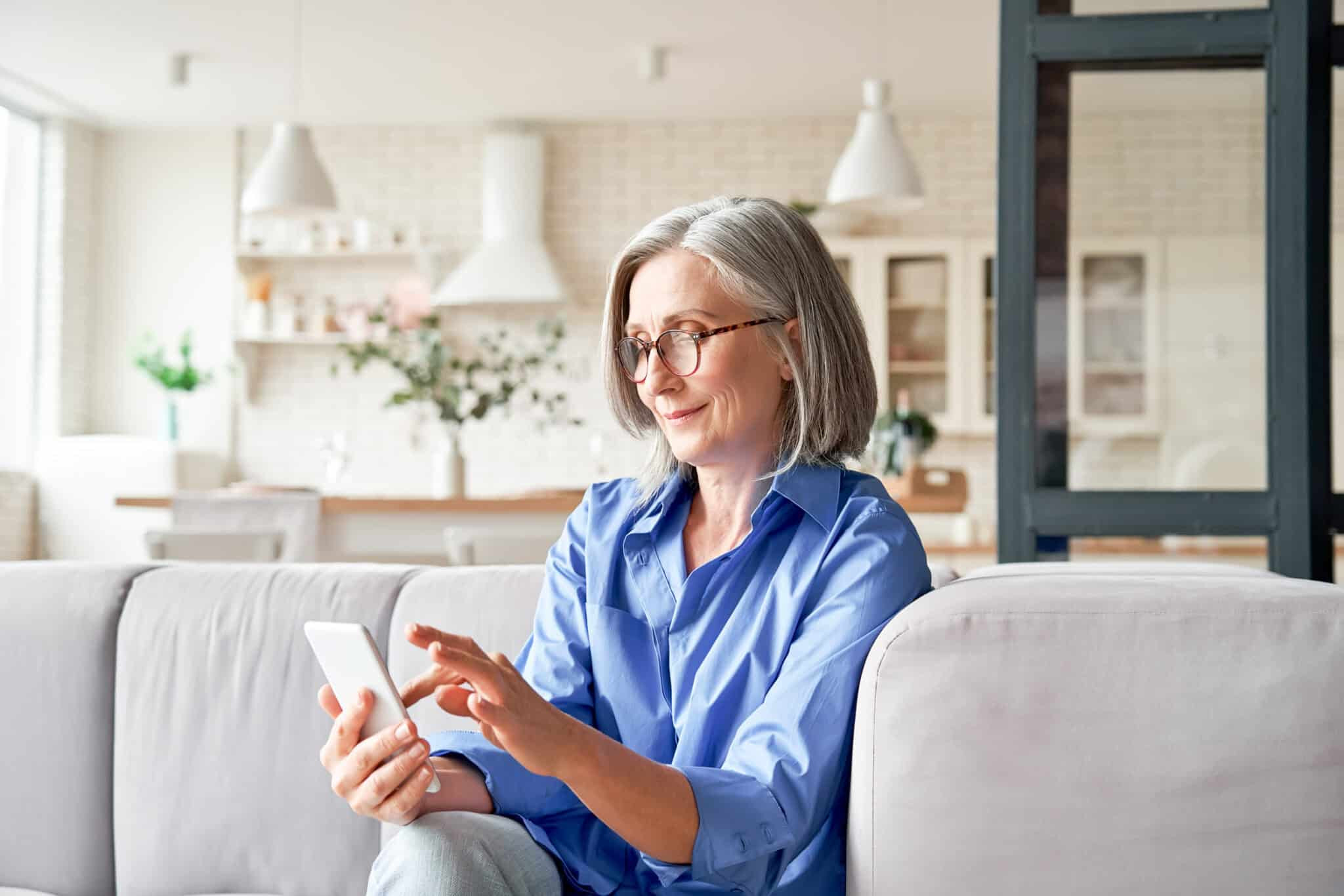 Older woman using a smartphone at home, managing personal tasks or healthcare information digitally.