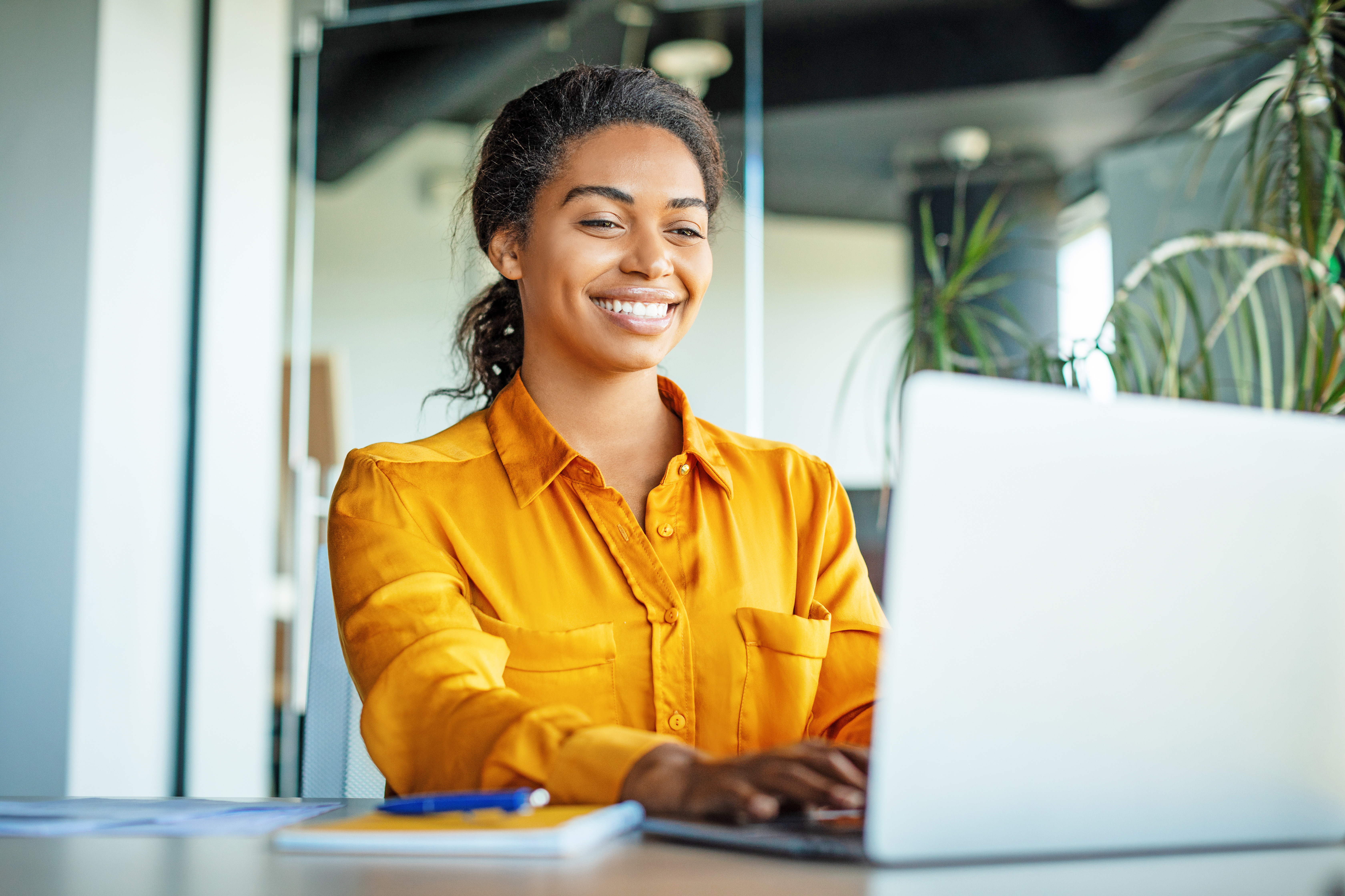 Happy black businesswoman using laptop typing and working online while sitting at workplace in office