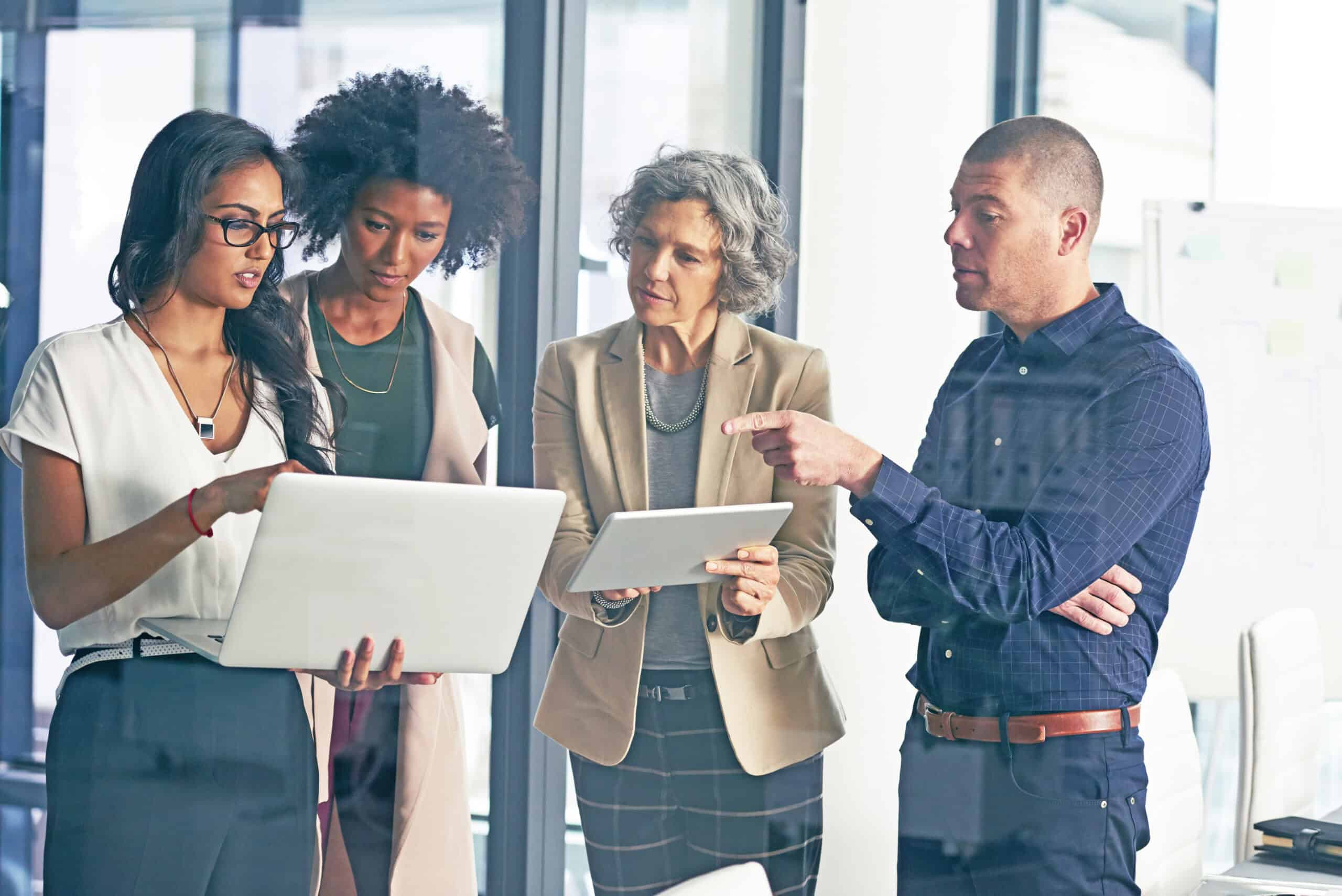 Business team collaborating around a laptop and tablet, discussing data and strategy in a modern office.