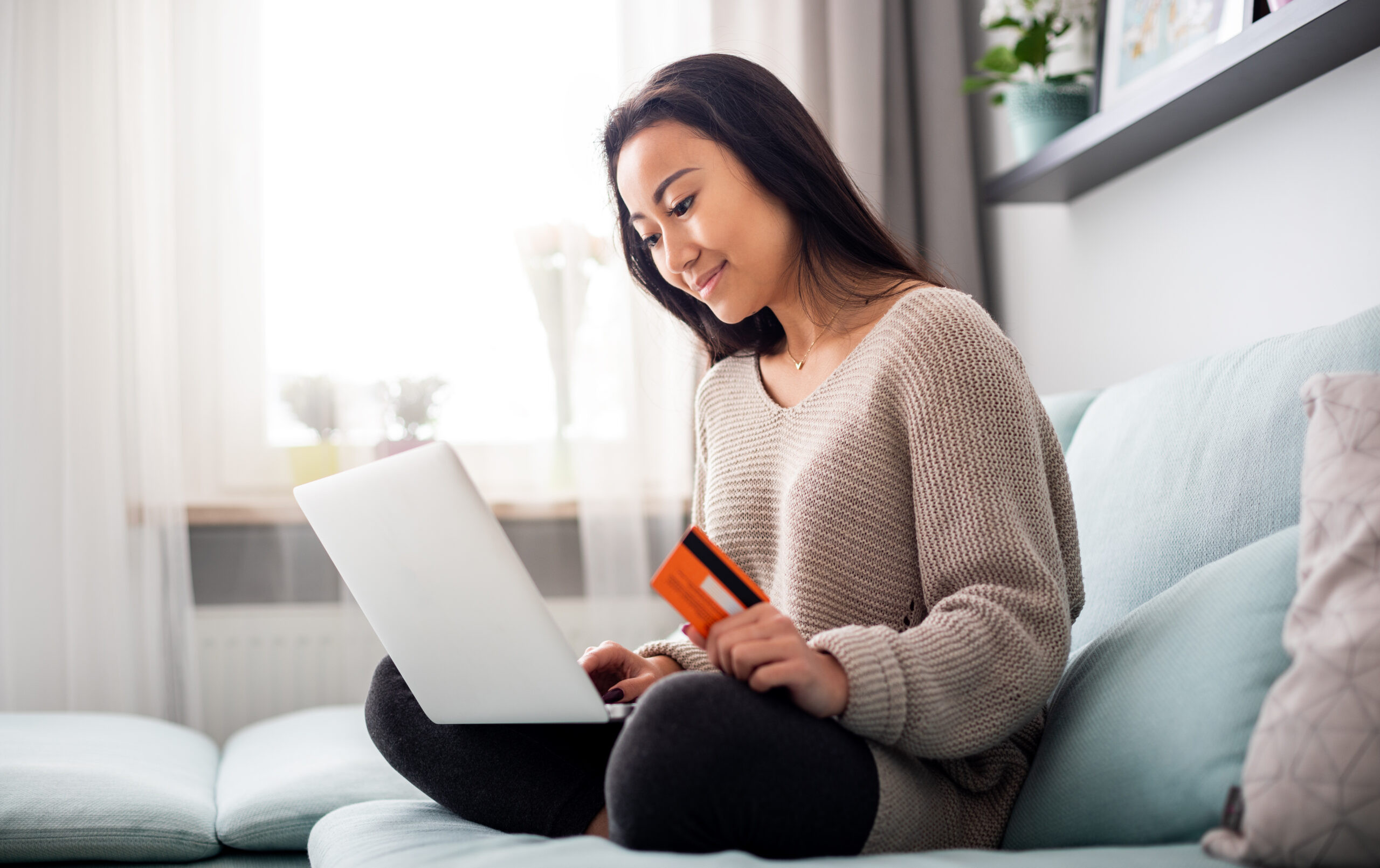 Woman using a laptop and credit card at home, representing online payments, digital billing, and convenient financial transactions.