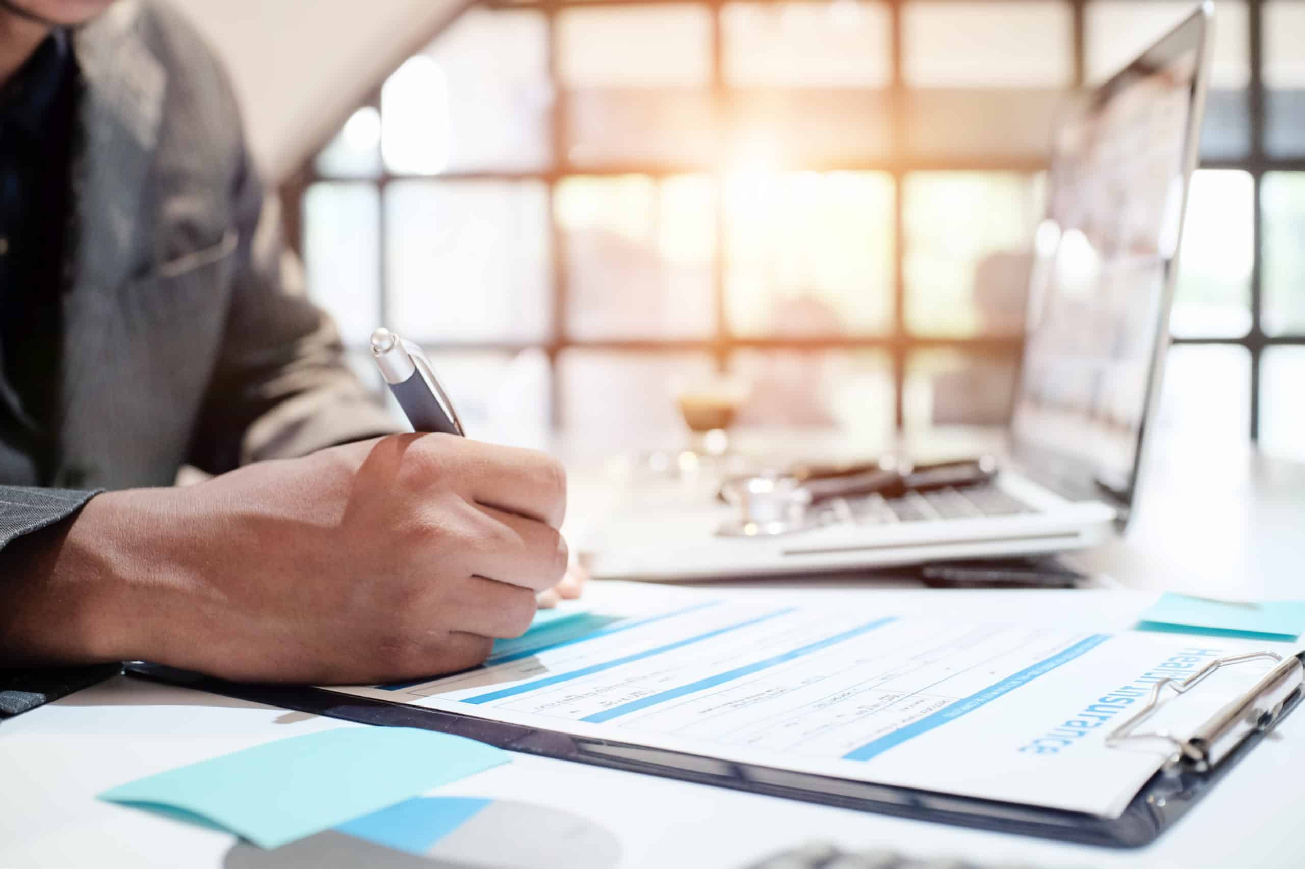 Professional completing financial paperwork on a clipboard with a pen at a desk, representing billing, documentation, and administrative workflows.