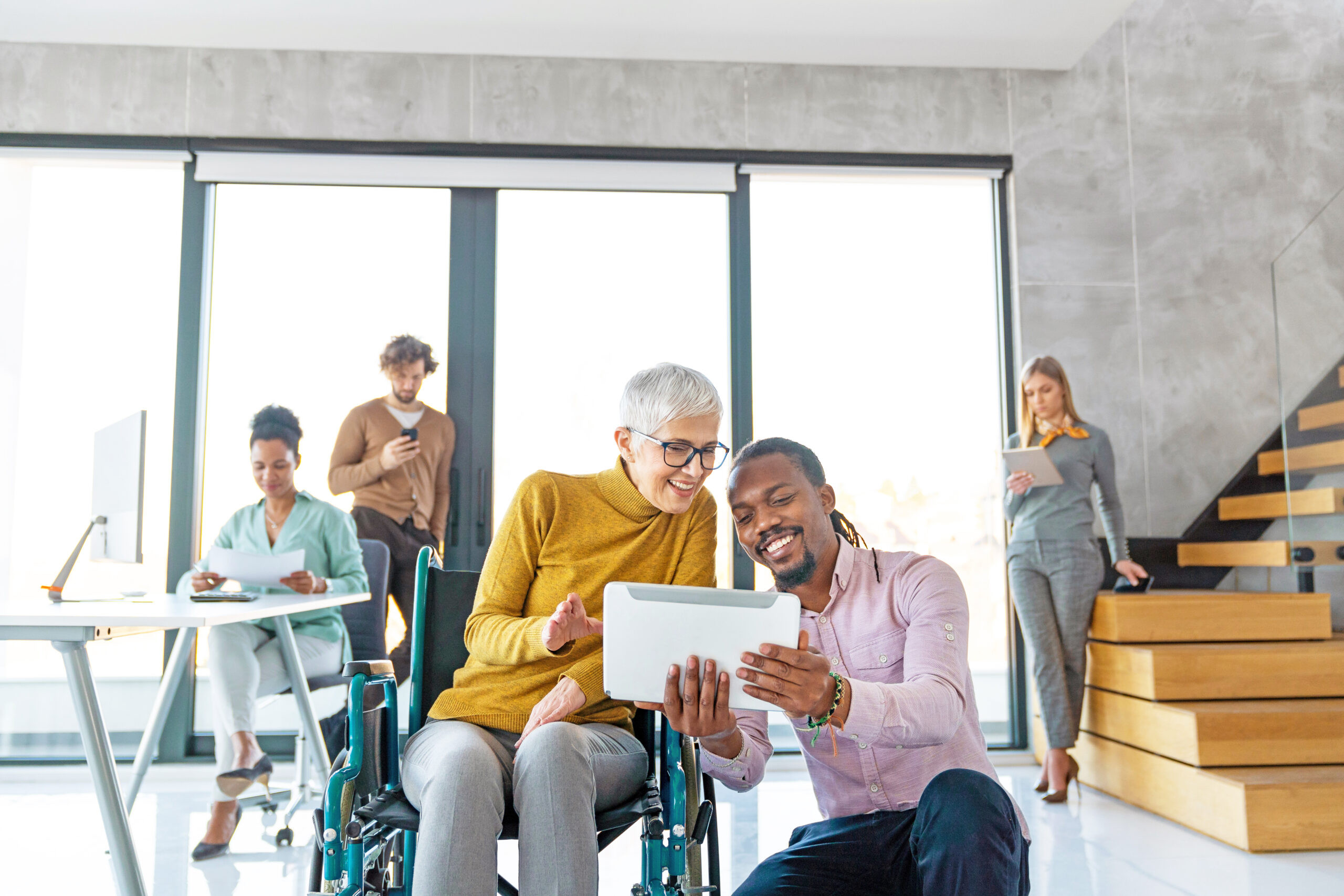 Diverse team collaborating in a modern office, including a wheelchair user, reflecting inclusive workplace culture and teamwork.