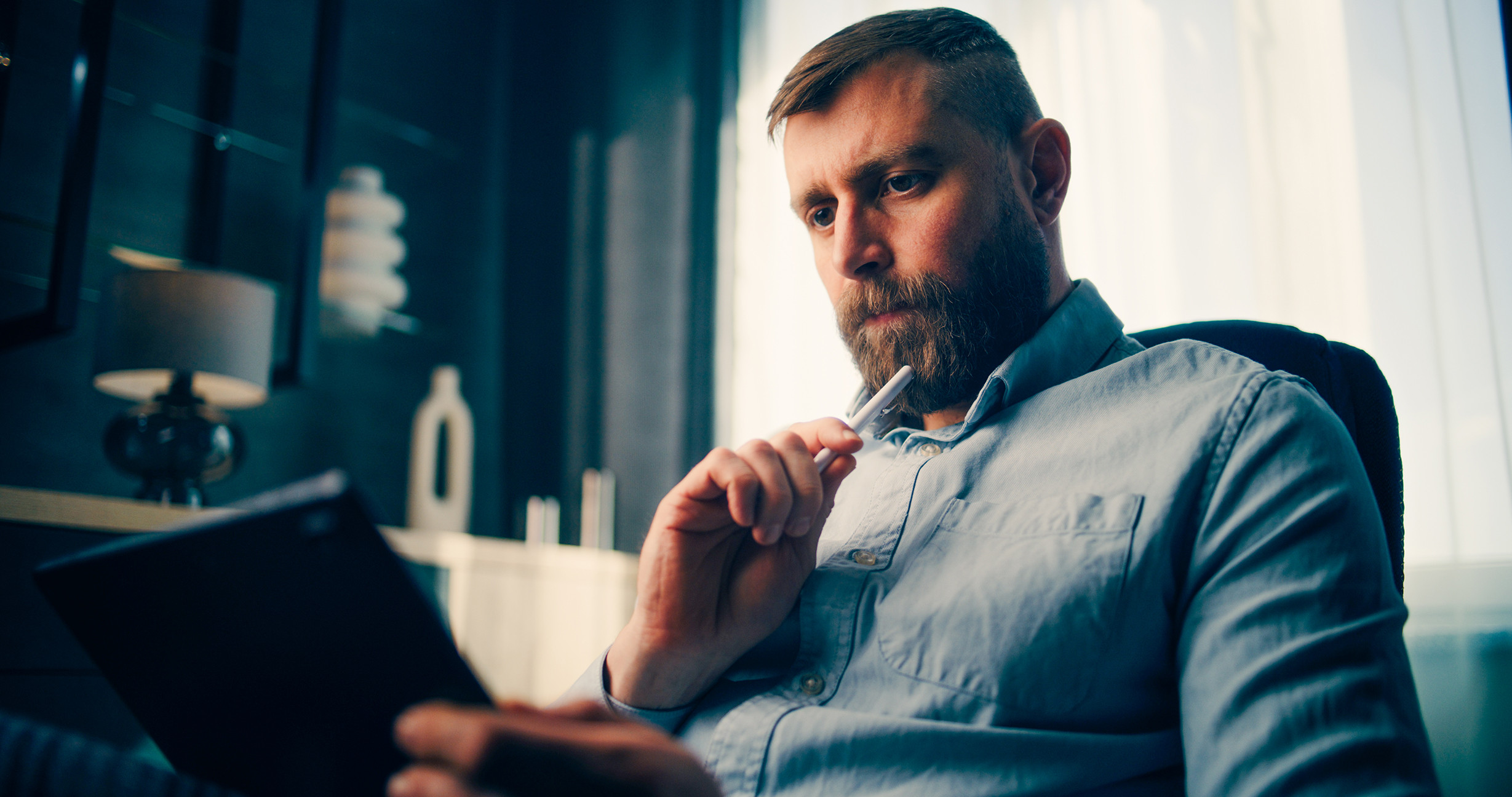 Business professional reviewing data on a tablet while thinking in a modern office.