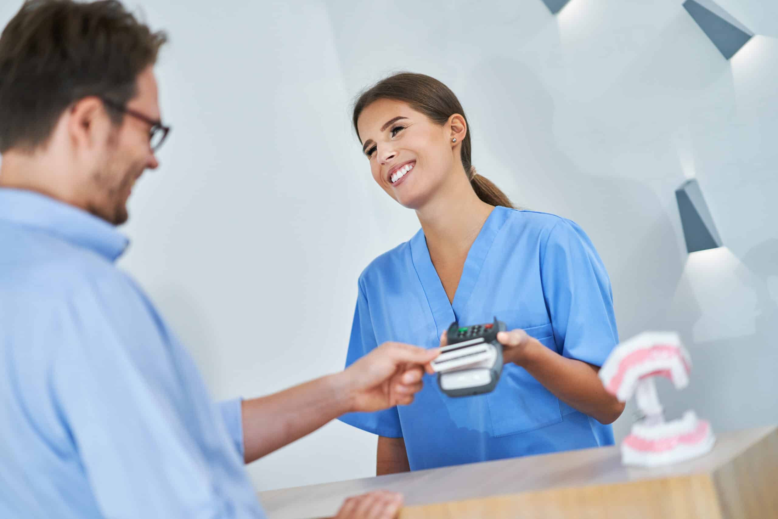 Patient making a contactless payment at a healthcare reception desk with a card reader.