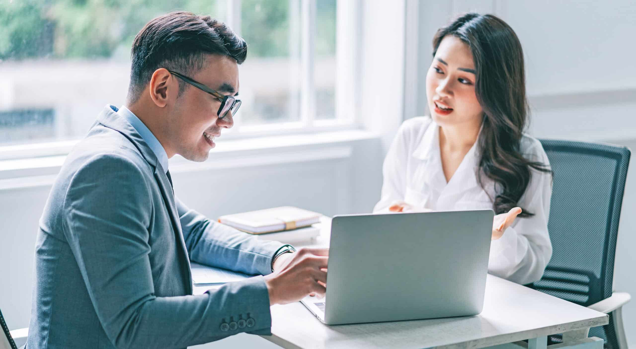 Two business professionals collaborating on a laptop during a meeting, discussing work in a modern office.