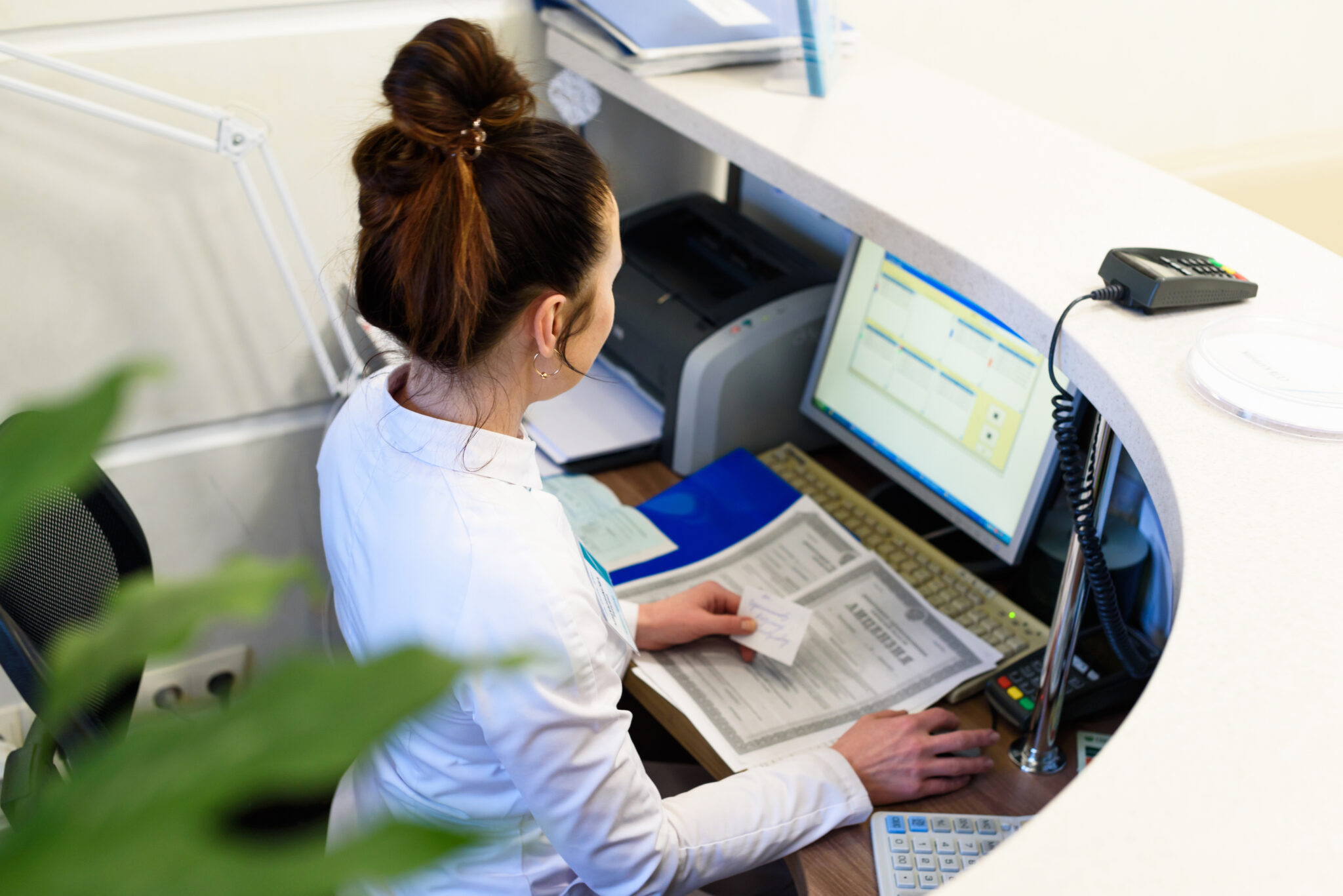 Healthcare staff member reviewing documents at a computer workstation in a hospital admissions area