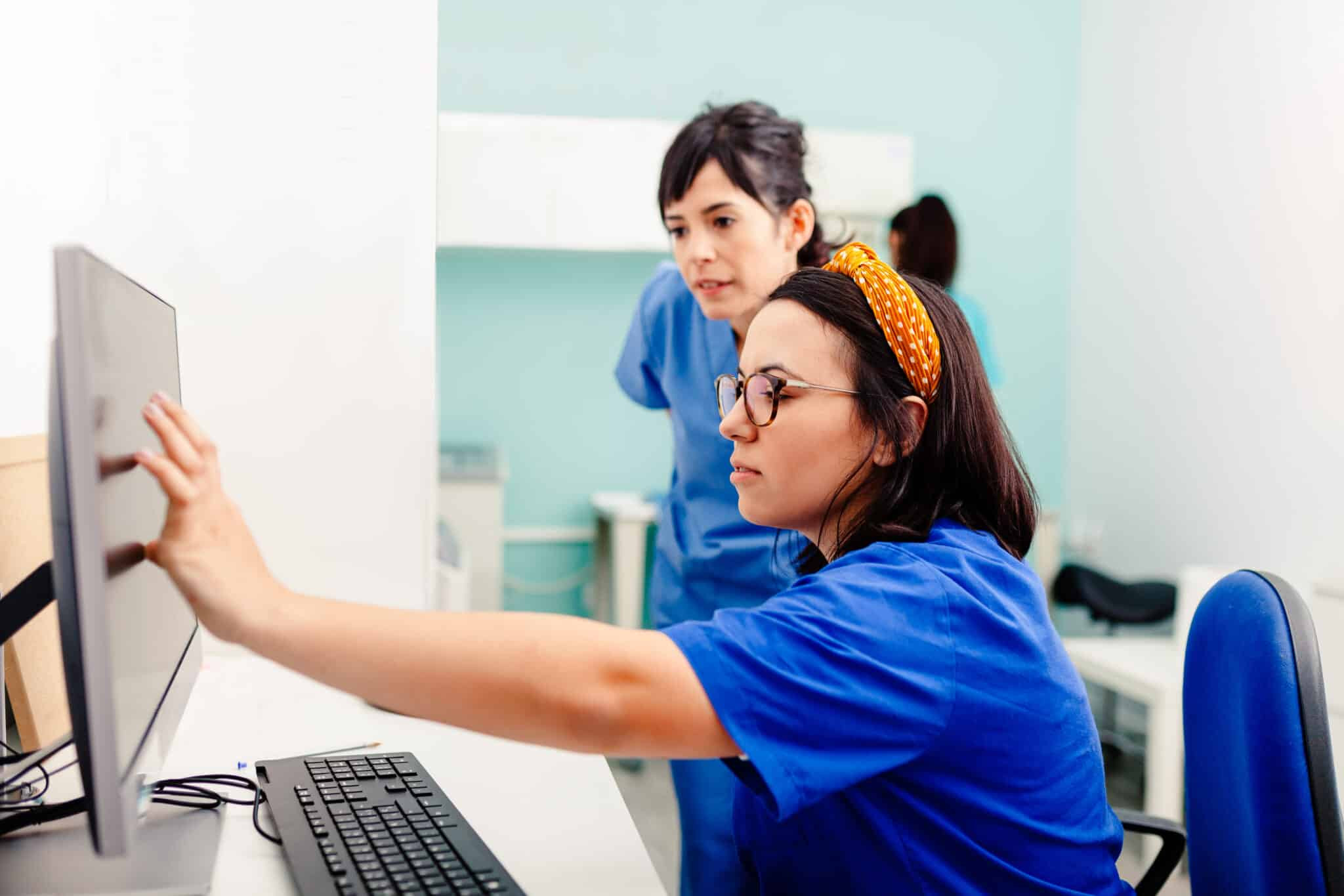 Healthcare professionals in scrubs using a computer to review patient information, supporting clinical workflows and digital health systems.