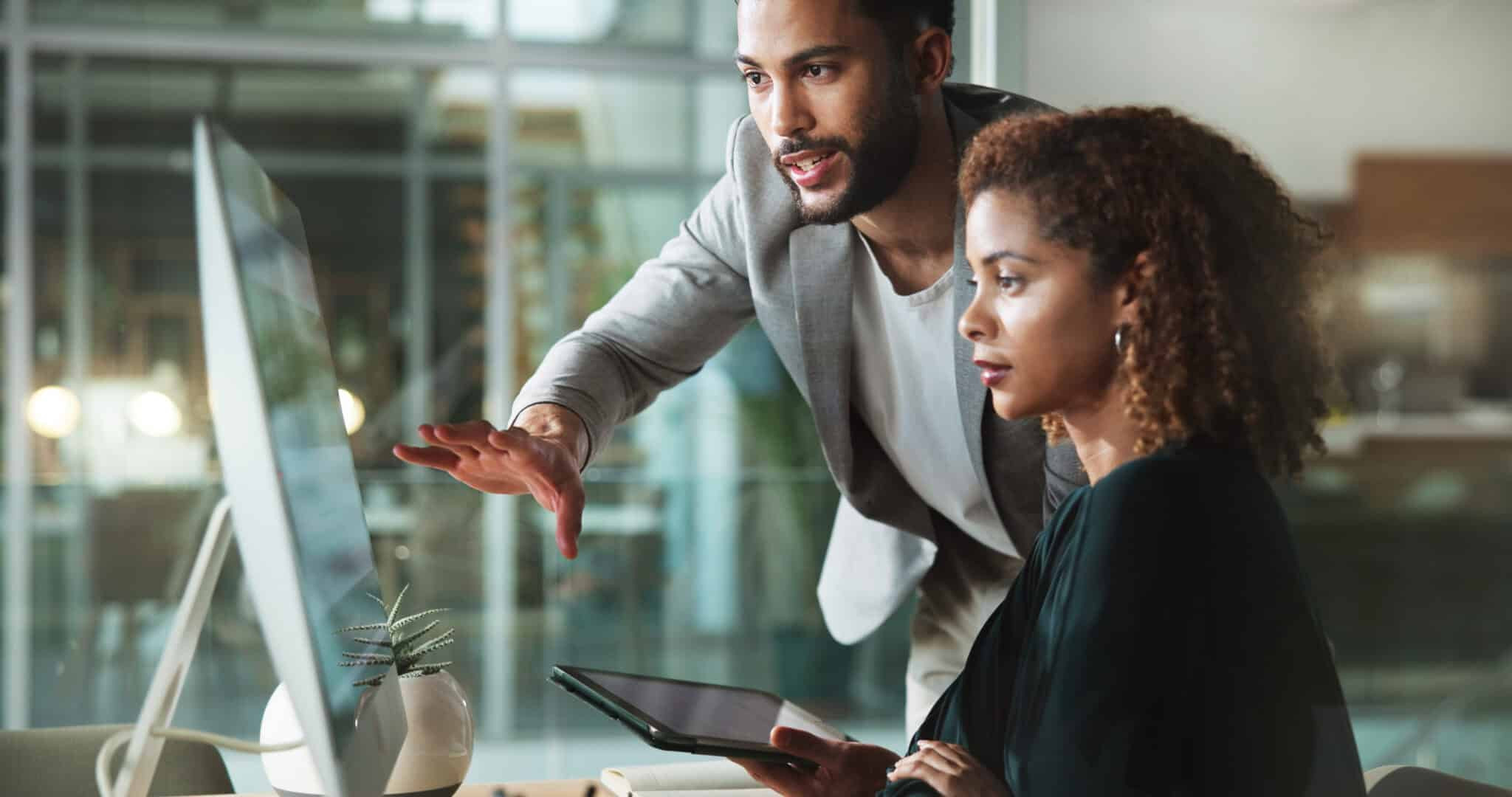 Two professionals reviewing information together on a desktop computer in an office
