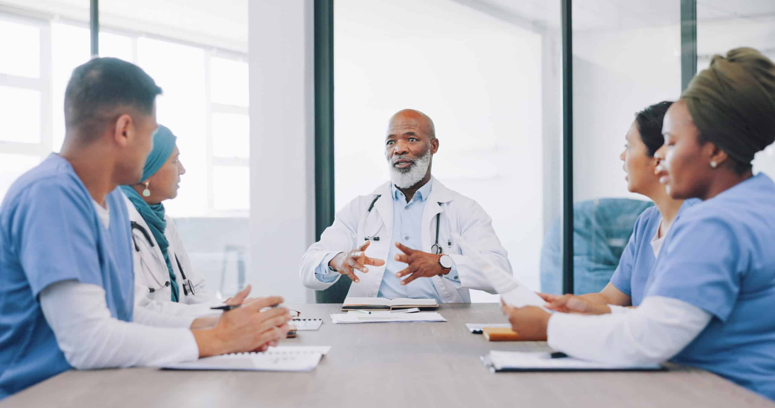 Senior physician leading a team meeting with healthcare professionals discussing patient care and clinical strategy.