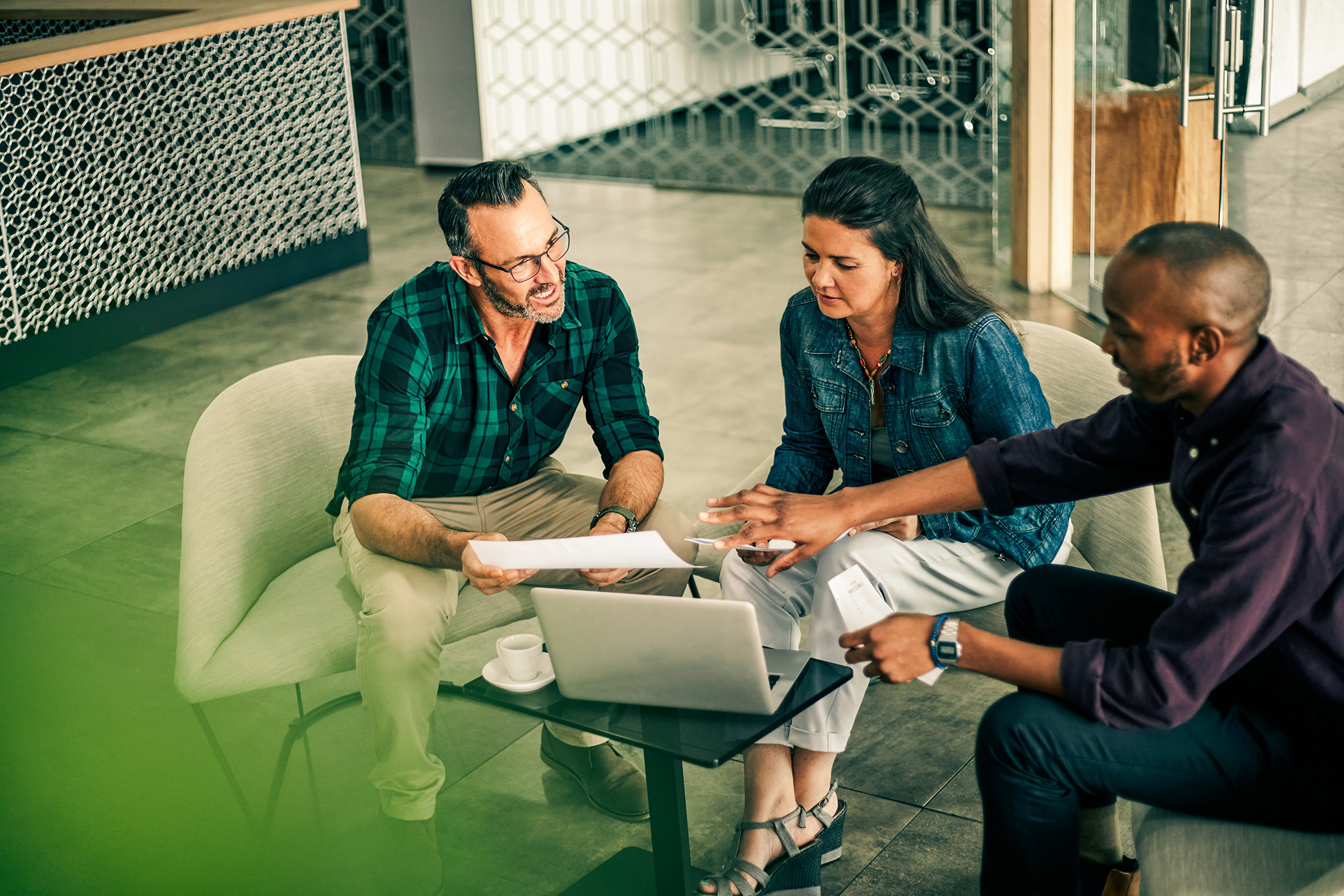Team of business professionals collaborating around a laptop, reviewing documents during a meeting.