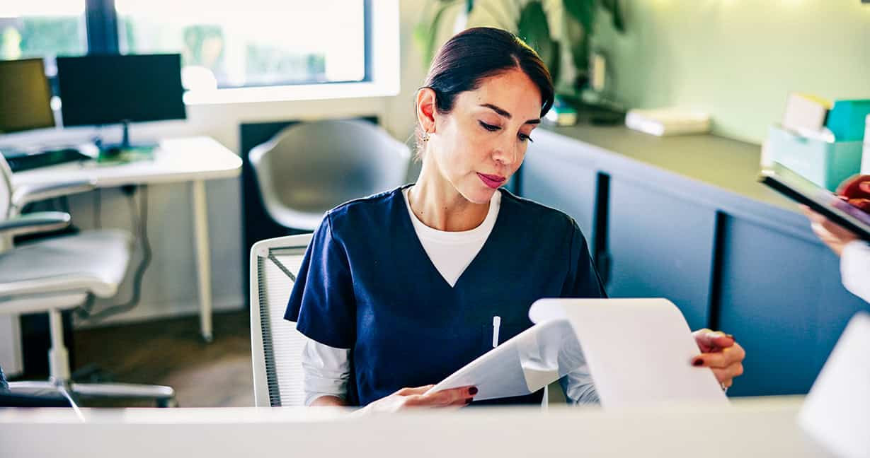 Healthcare administrative professional reviewing patient documents at a clinic front desk.