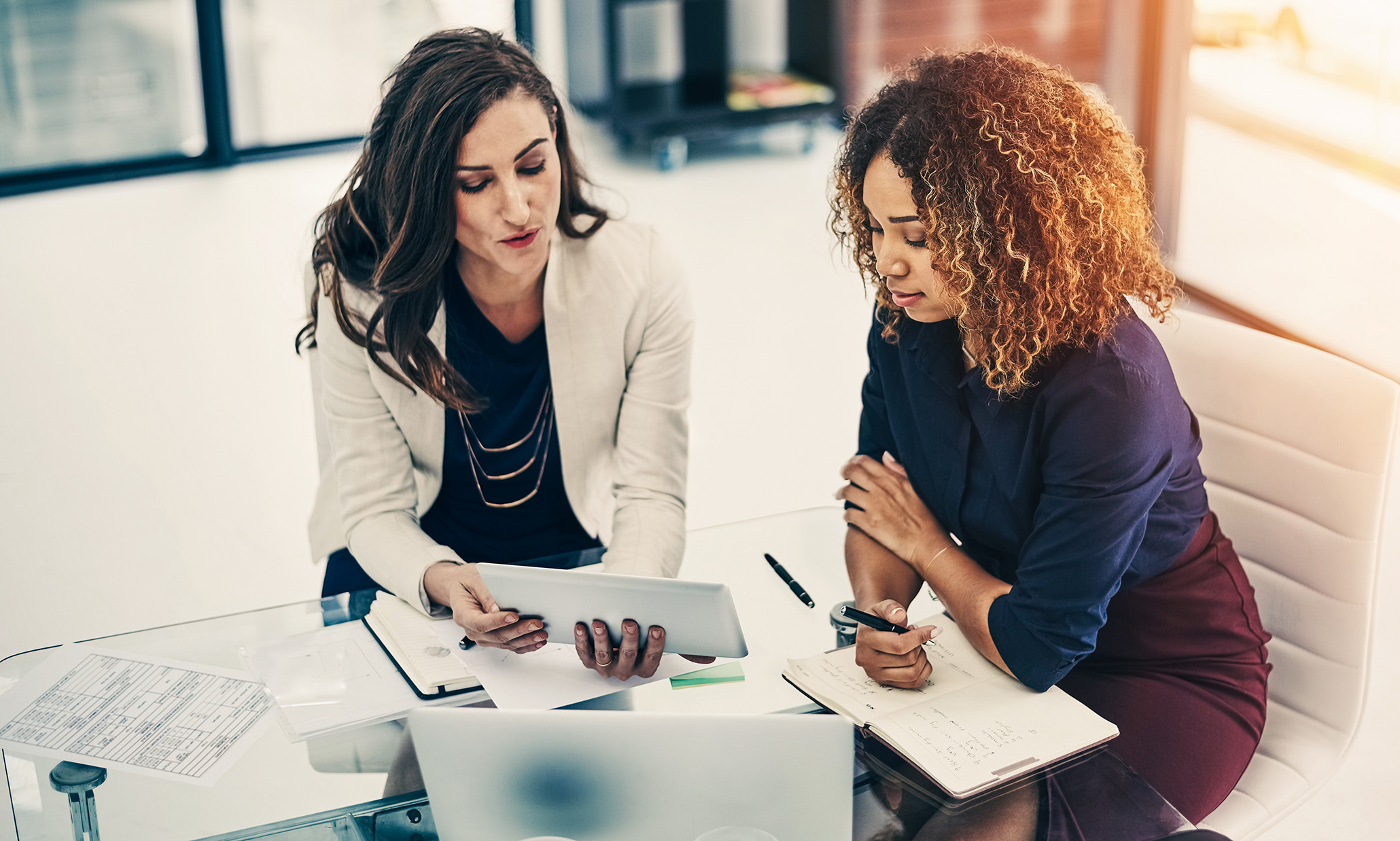 Two business professionals reviewing data on a tablet during a meeting, collaborating on analysis in an office setting.