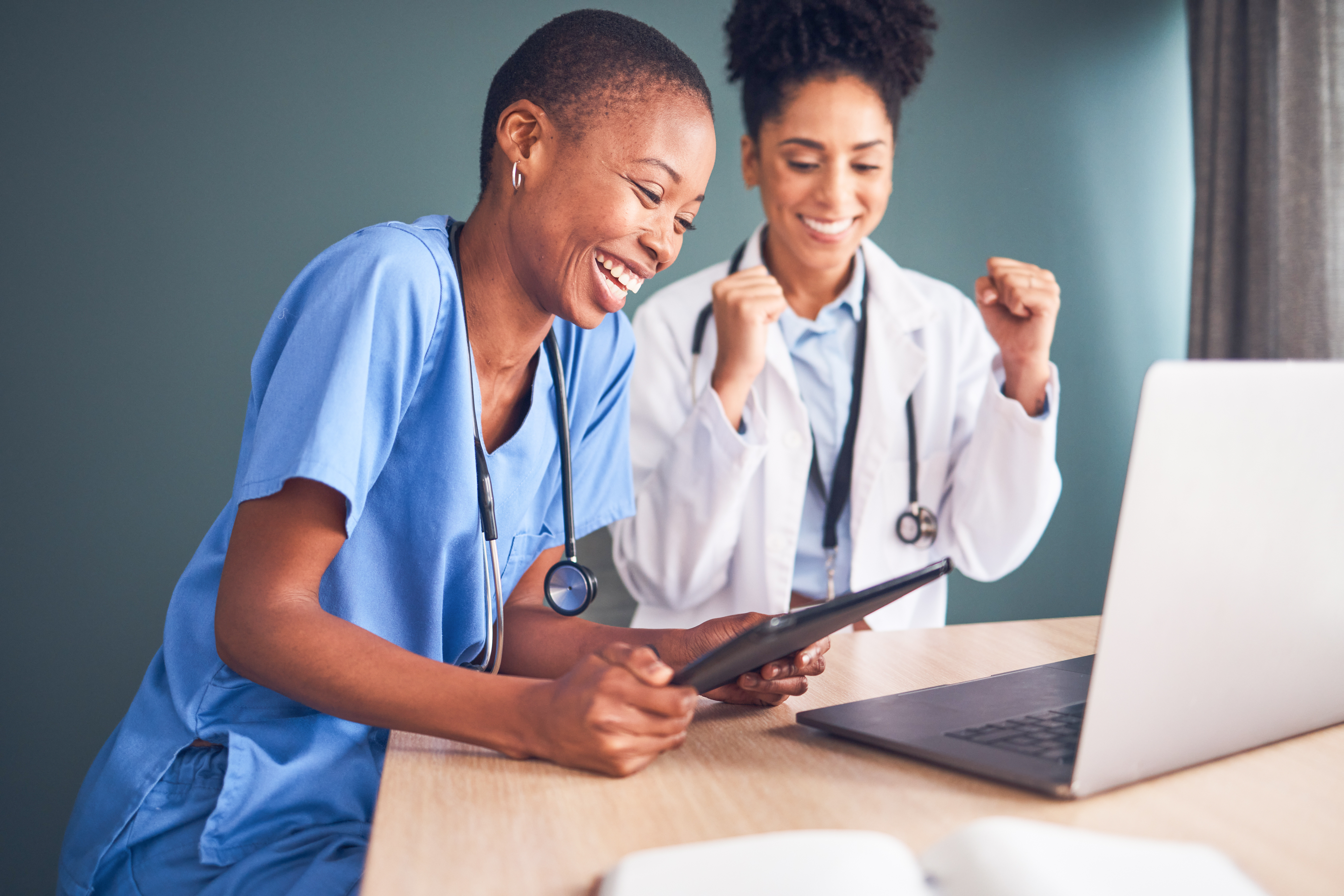 Healthcare professionals celebrating while reviewing data on a tablet and laptop, highlighting successful clinical outcomes and collaboration.
