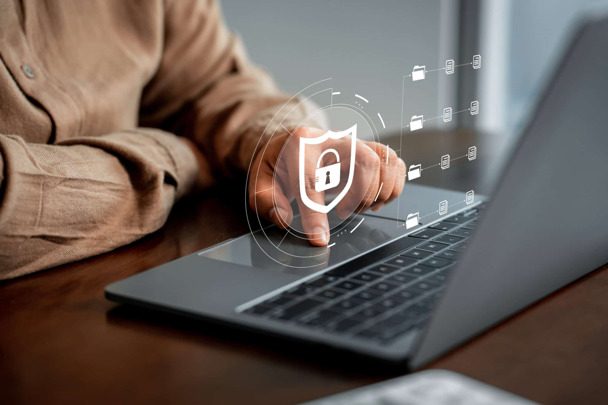 User interacting with a laptop displaying a security shield icon, representing cybersecurity, data protection, and secure digital systems.