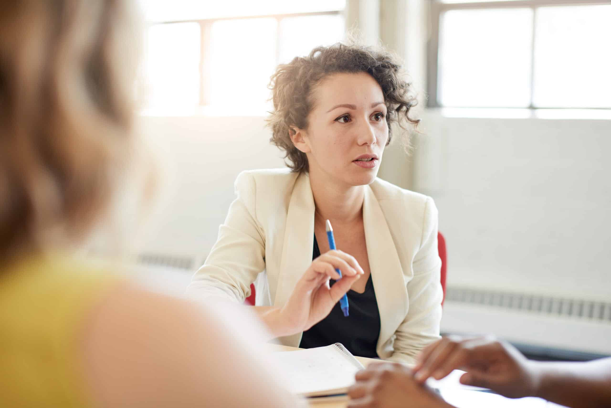 Business professional leading a discussion during a team meeting, holding a pen and taking notes.