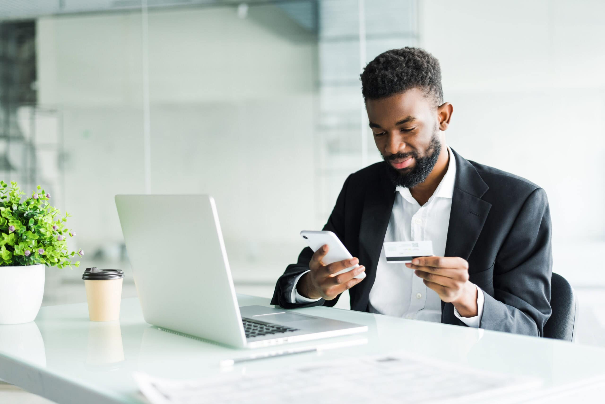 Professional using a smartphone and credit card at a laptop, representing digital payments, billing, and financial transactions.