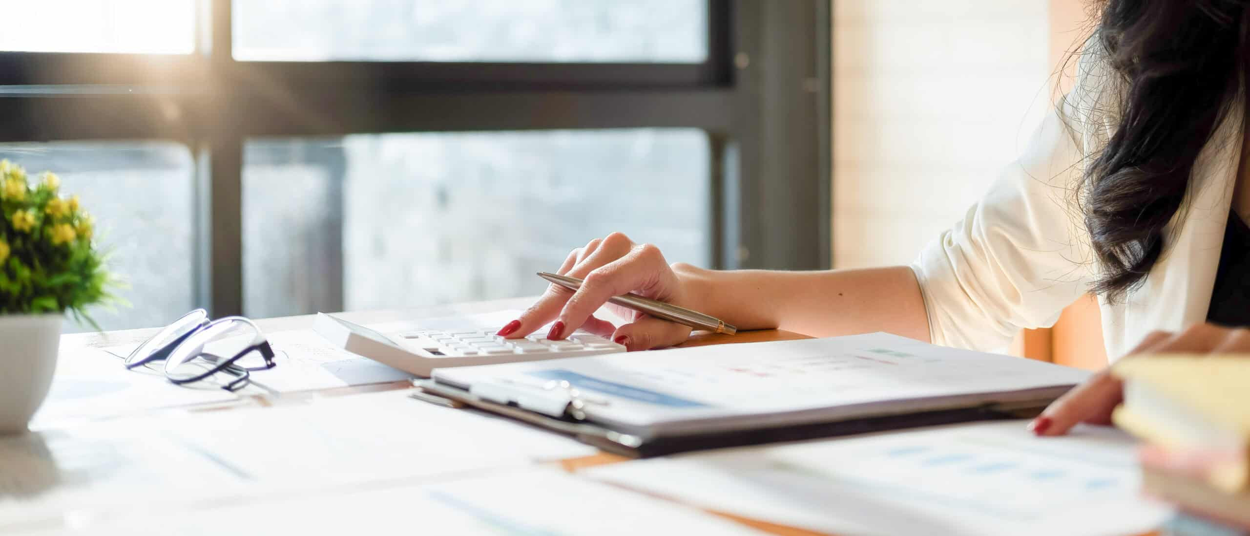 Professional reviewing financial documents and using a calculator at a desk, representing accounting, billing, and financial analysis.