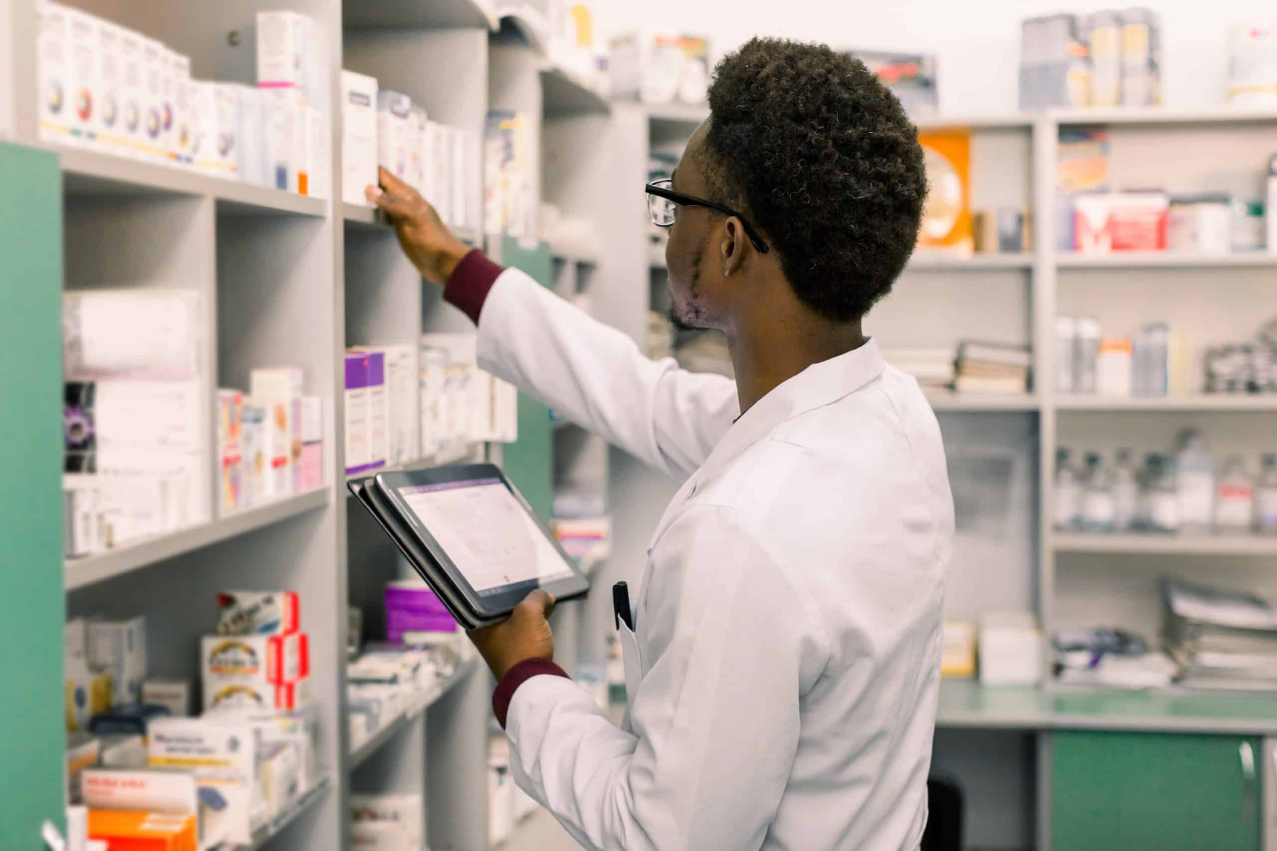 African American male pharmacist using digital tablet during inventory in pharmacy.|