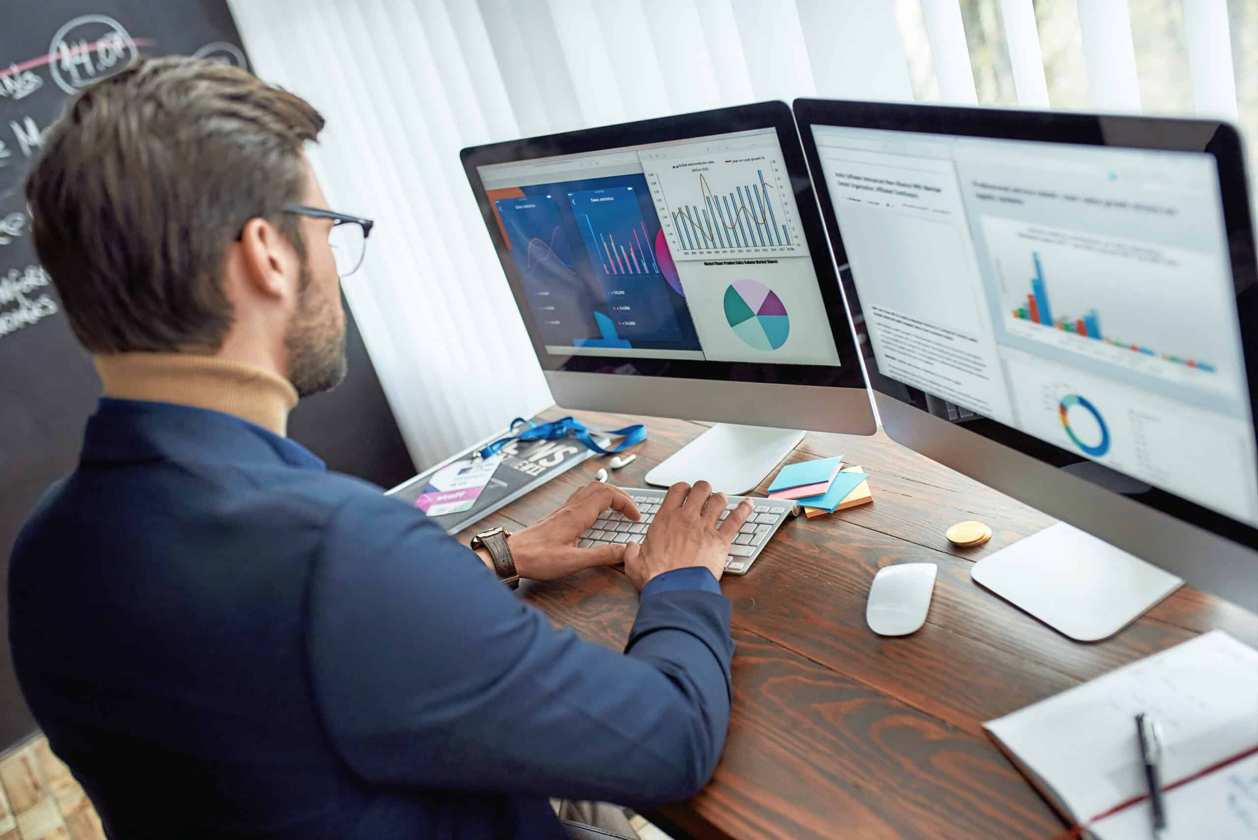 Preparing report. Rear view of focused businessman or financial analyst working in the modern office, looking at graphs and charts on pc screen, analyzing statistical data